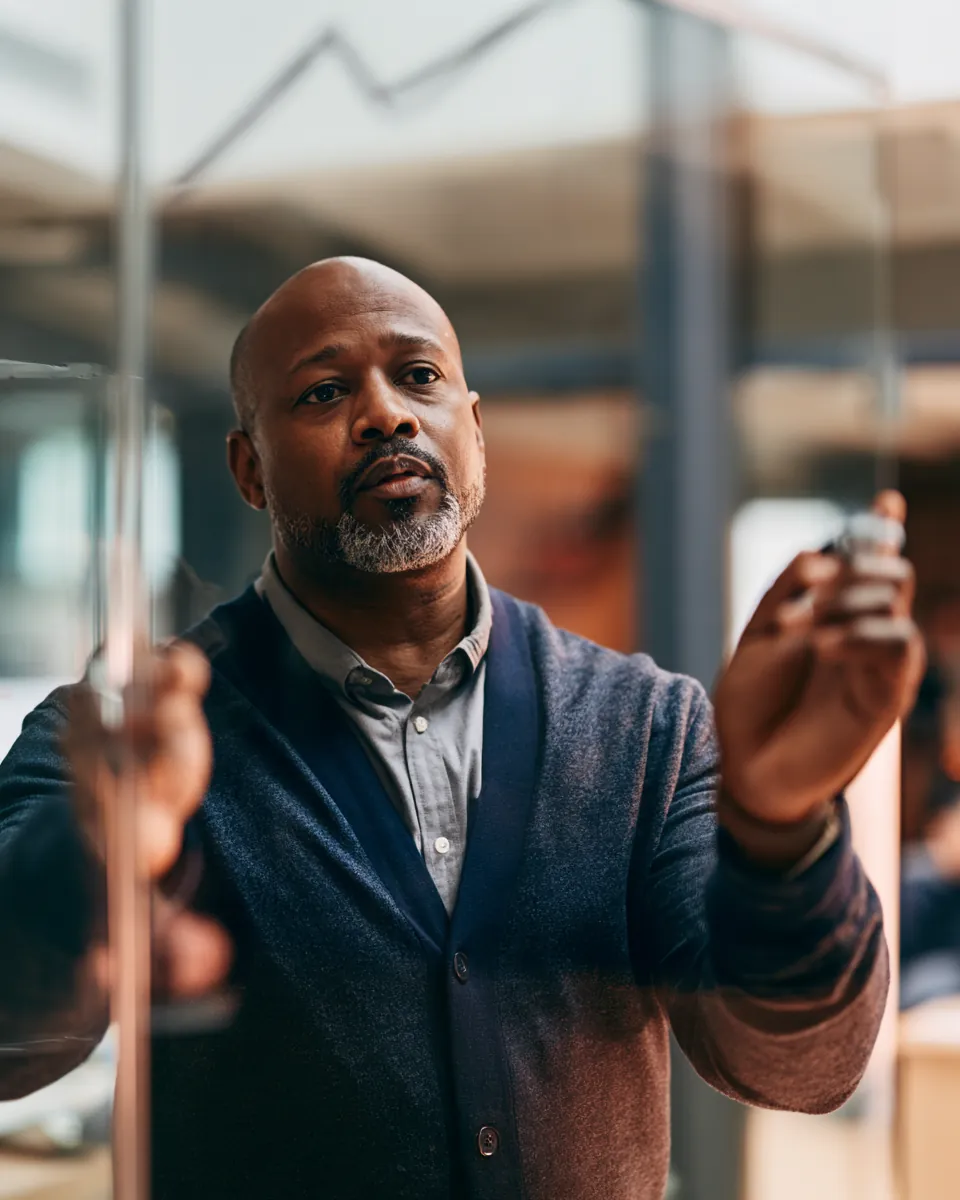 Advisor sketching a rising line graph on a glass wall while explaining personal loan rates